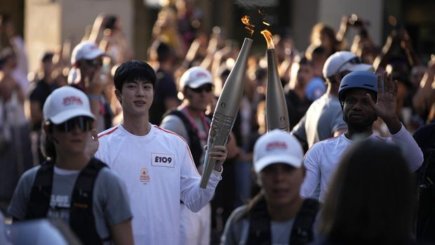 Dok. Jin, member tertua supergrup K-pop BTS, membawa obor Olimpiade, Minggu, 14 Juli 2024 di Paris. (AP:Louise Delmotte)